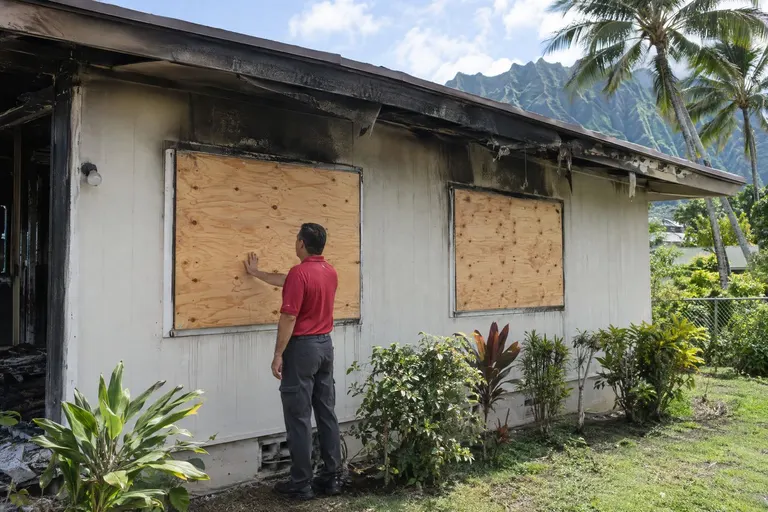 Plywood boarded over smoke-stained windows of a home after a fire,.