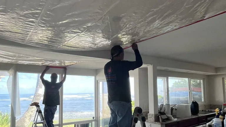 A technician on a ladder covering a water-damaged ceiling in an oceanfront home.