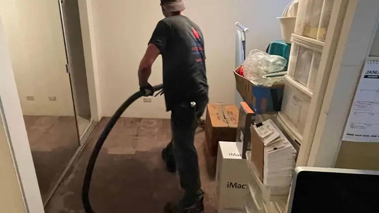 A technician extracting standing water from a carpeted room with a truck-mounted hose.