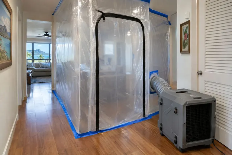 A plastic containment area with a zipper door and an air scrubber exhausting through ducting in a home.