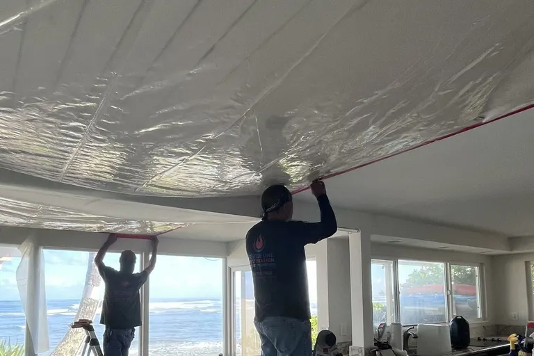 A restoration worker on a ladder covering a water-damaged ceiling