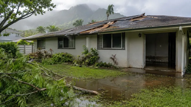 A single-story home with storm debris and standing water in the yard after heavy rain.