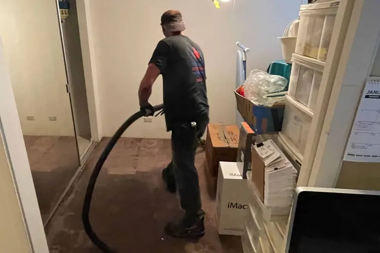 A technician pulling standing water out of a carpeted room with an extraction hose.